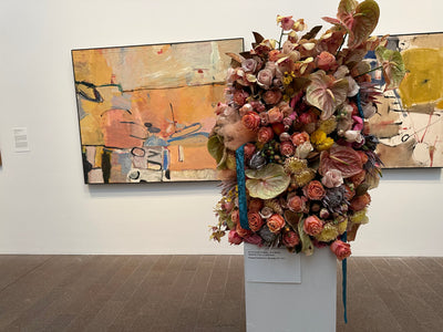 Floral arrangement on a pedestal in an art gallery with abstract paintings in the background