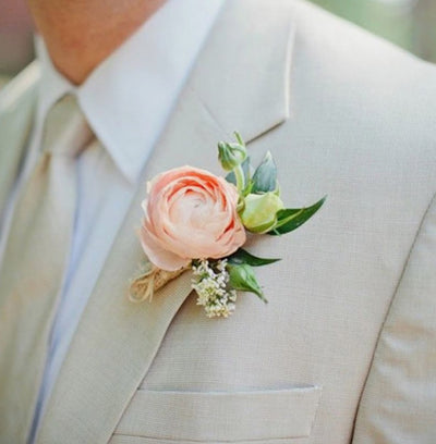 a perfect boutonniere of a peach ranunculus on a tan jacket lapel