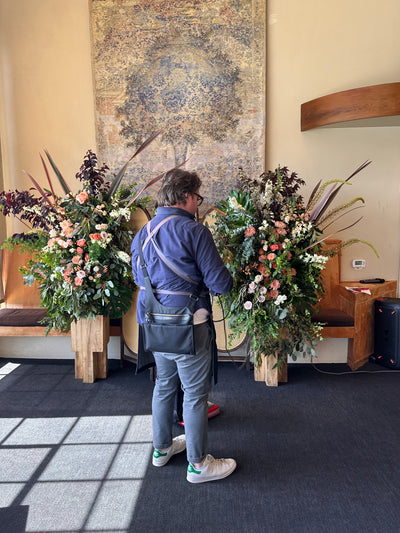 wooden pedestals hold tall swoops sculptural floral arrangements for a ceremony backdrop